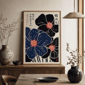 Peut inclure: Une affiche encadrée représentant des fleurs stylisées bleues et noires avec des centres rouges sur fond crème. Du texte japonais est visible dans les coins supérieurs. L'œuvre est exposée sur une surface en bois.