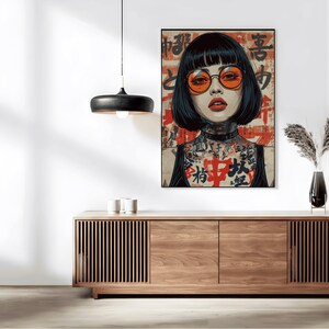 K&ouml;nnte beinhalten: Ein gerahmter Kunstdruck mit einer Frau mit schwarzen Haaren und orangefarbenen Gl&auml;sern. Das Kunstwerk hat eine japanische &Auml;sthetik mit rotem und schwarzem Text im Hintergrund und T&auml;towierungen am Hals und an der Brust der Frau. Der Druck wird &uuml;ber einem Holzschrank ausgestellt.