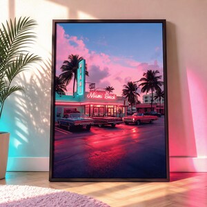 Op de afbeelding: Ingelijste print van een Miami Beach-scène bij zonsondergang. De afbeelding toont een retro diner met een neonreclame, palmbomen en klassieke auto's. De lucht is een mix van roze, blauwe en paarse tinten, die reflecteren op het natte wegdek.