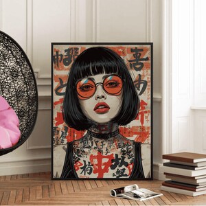 K&ouml;nnte beinhalten: Gerahmter Kunstdruck mit einem Portr&auml;t einer Frau mit schwarzen Haaren, orangefarbener Brille und rotem Lippenstift. Das Kunstwerk enth&auml;lt japanischen Text und T&auml;towierungen. Der Druck ist in einem schwarzen Rahmen und wird in Innenr&auml;umen ausgestellt.