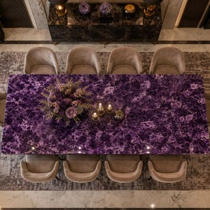 May include: A rectangular dining table with a polished purple amethyst gemstone surface, surrounded by ten beige upholstered chairs. A floral centerpiece and three glass candle holders are placed on the table, viewed from a high-angle perspective.