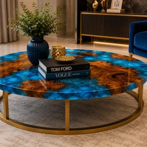 May include: A round coffee table featuring a glossy surface with a swirling pattern of deep blue and natural wood tones. The table is supported by a circular gold metal frame. On top sit a dark blue vase, a gold bowl, and two books labelled Tom Ford and Vogue.