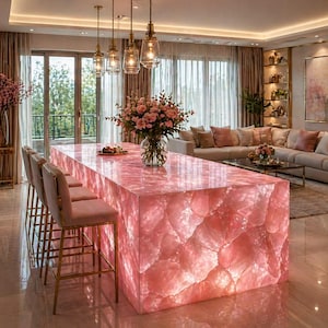 May include: A luxurious kitchen island made of pink quartz, illuminated from within. The island features a textured surface and is paired with pink velvet bar stools with gold legs. Overhead, three pendant lights hang above the island, illuminating the space.