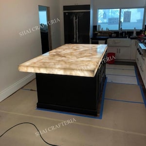May include: A kitchen island with a black base and a glowing, light-colored countertop. The countertop has a marbled appearance. The words "SHAI CRAFTERIA" are visible in the image.