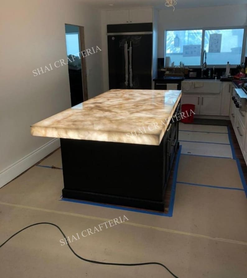 May include: A kitchen island with a black base and a glowing, light-colored countertop. The countertop has a marbled appearance. The words "SHAI CRAFTERIA" are visible in the image.