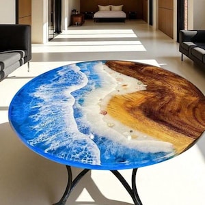 May include: A round table featuring a natural wood grain surface on one side and a blue resin ocean design on the other. The resin depicts white crashing waves meeting a sandy shore with small embedded seashells, supported by a black metal base.