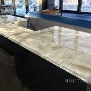 May include: An L-shaped countertop with a light-colored, translucent surface. The countertop is set on a dark gray cabinet. The text "SHAI CRAFTERIA" is visible on the countertop.