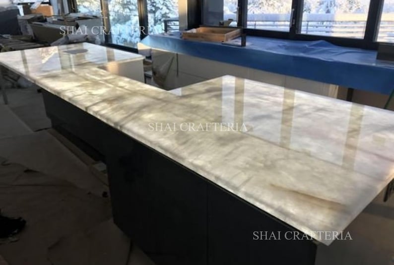 May include: An L-shaped countertop with a light-colored, translucent surface. The countertop is set on a dark gray cabinet. The text "SHAI CRAFTERIA" is visible on the countertop.