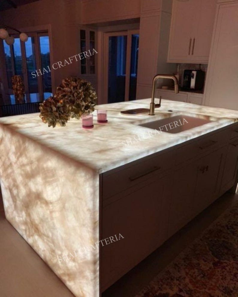 May include: A backlit kitchen island with a marble countertop and a built-in sink. The island has a light brown cabinet base with a gold faucet. The countertop has a natural stone pattern. The text "SHAI CRAFTERIA" is visible.