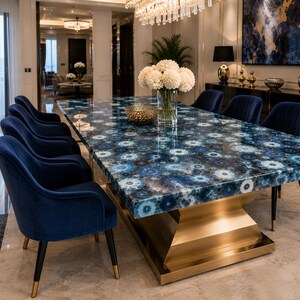 May include: A rectangular dining table with a polished blue agate stone top featuring circular patterns, supported by a wide, brushed gold metal pedestal base. The table is surrounded by several navy blue velvet chairs with black legs.
