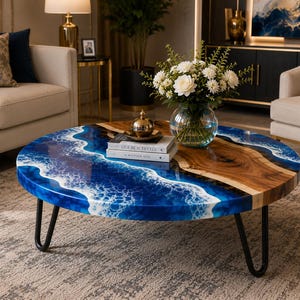 May include: A circular coffee table featuring a blue resin design mimicking ocean waves. It has a natural wood grain section and black metal hairpin legs. Books and a decorative object are on the table.