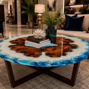 May include: A round coffee table featuring a natural wood slab centre with a glossy resin finish. The resin border displays swirling shades of blue and white, mimicking ocean waves. The table is supported by a dark brown, X-shaped metal base.