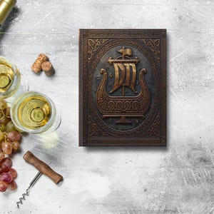 Puede incluir: Un libro decorativo con un diseño en relieve detallado de un barco vikingo. El libro es marrón y dorado, con una apariencia texturizada. La imagen también incluye copas de vino, una botella de vino, uvas y un sacacorchos.