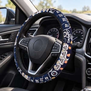 May include: A dark blue steering wheel cover featuring a repeating pattern of the text Briar, the number 44, the number 22, the number 66, and the script text Off Campus, installed on a black steering wheel inside a vehicle interior.