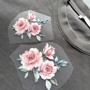 May include: Two floral iron-on patches with pink watercolour roses and green and blue leaves. The patches are displayed on a grey t-shirt, demonstrating the design's application.