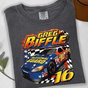 May include: Pepper-colored t-shirt featuring a graphic of a race car with the text "GREG BIFFLE" in a flame design. The car is blue, red, and yellow with the words "NATIONAL GUARD" and the number "16".