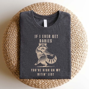a gray t-shirt with a raccoon graphic and text printed on it.
