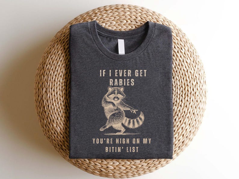a gray t-shirt with a raccoon graphic and text printed on it.