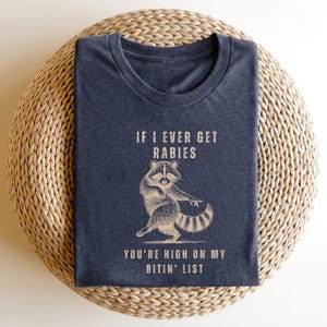 a blue t-shirt with a graphic of a raccoon and text that reads "If I ever get Rabies, you're high on my bitin' list".