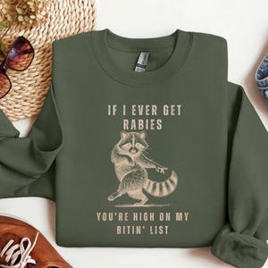 a green sweatshirt with a raccoon graphic and text, along with some other clothing items and accessories.