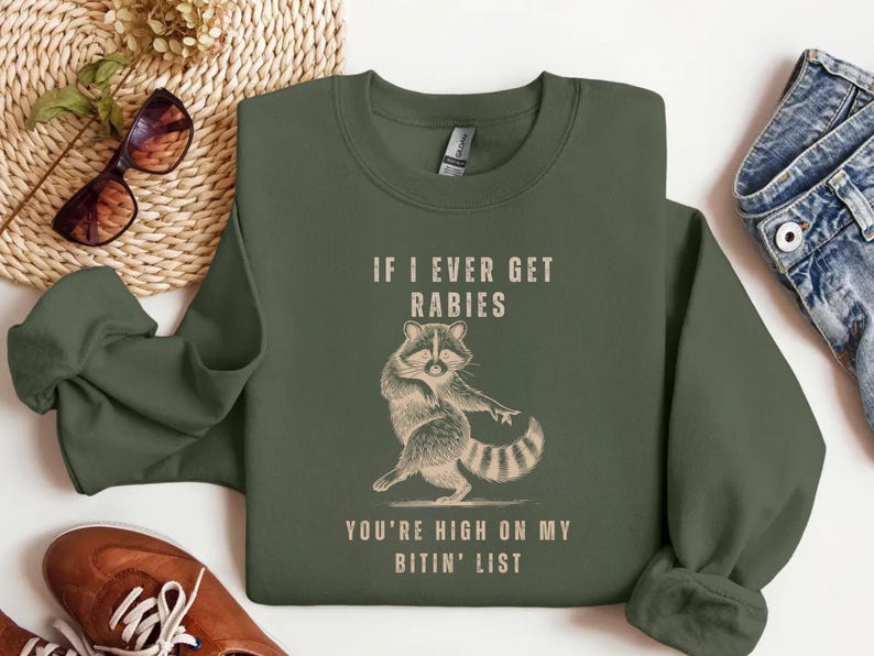 a green sweatshirt with a raccoon graphic and text, along with some other clothing items and accessories.