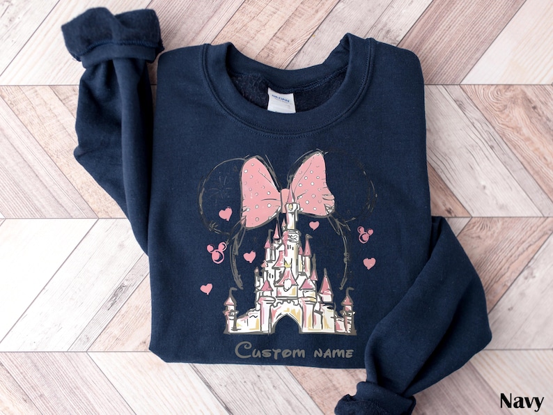 A navy blue sweatshirt with a pink bow and a castle graphic printed on it, along with the text "Custom Name" printed below the castle.