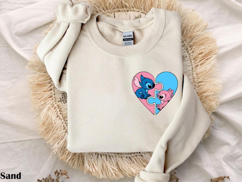 A beige sweater with a heart-shaped design featuring two cartoon characters, one blue and one pink, on the front.