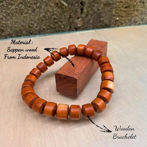 May include: A wooden bracelet made of Sappan wood from Indonesia. The bracelet features cylindrical beads in varying shades of brown and tan. The text "Wooden Bracelet" is visible in the image.