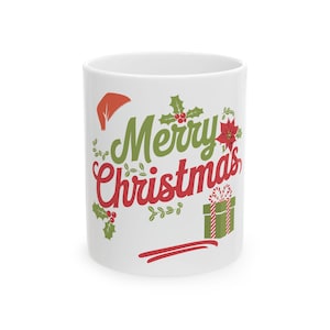 Puede incluir: Taza de cerámica blanca con las palabras "Merry Christmas" en letras verdes y rojas. La taza está decorada con acebo festivo, un gorro de Papá Noel, una flor de Pascua y un regalo envuelto. Un regalo de vacaciones perfecto.