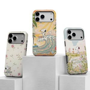 May include: Three phone cases with different designs. One case features Snoopy surfing a wave, another has a floral pattern with Snoopy, and the third depicts Snoopy near a pond. All cases have a white camera section.