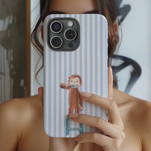 May include: A phone case with a blue and white striped pattern. The case features a cartoon illustration of a brown monkey brushing its teeth while standing on a small blue stool. The phone case has a black camera module.