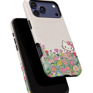 Może przedstawiać: Etui na telefon z kwiatowym wzorem i postacią z kresk&oacute;wki. Etui ma białe tło z kolorową kwiatową obw&oacute;dką. Postać z kresk&oacute;wki ma na sobie r&oacute;żową kokardę i sukienkę.