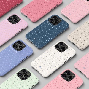 May include: A selection of phone cases in shades like pink, blue, and white, all decorated with a polka dot design. Each case has a smooth surface and displays the initials "AC".