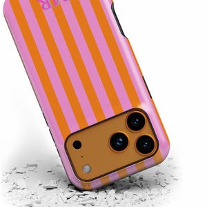 May include: A pink and orange striped phone case with the letters "MR" in the upper left corner. The case has a camera cutout with three lenses and a flash. The case is lying on a white surface.