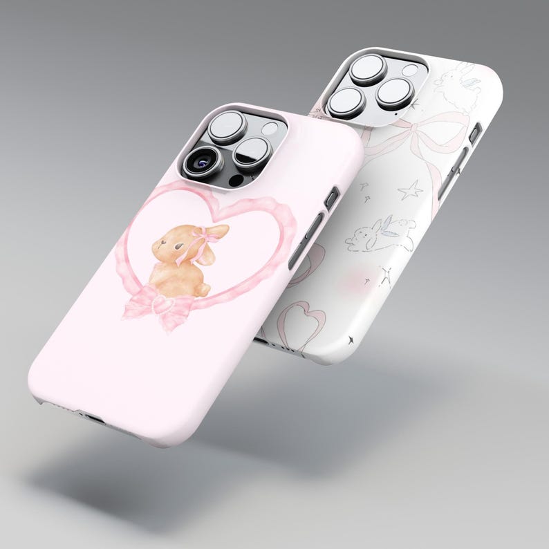 May include: Two phone cases. One is light pink with a watercolor bunny inside a heart-shaped frame. The other is white with a pattern of bows, stars, and bunnies. Both cases have a glossy finish.