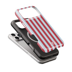 May include: A smartphone with a black case and a striped red and light blue phone case. The striped case has the initials "MR" in white. The phone is silver.