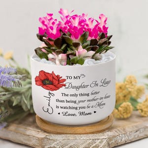 May include: A white ceramic planter with a vibrant pink and green succulent arrangement. The planter features a red poppy illustration and the text "TO MY Daughter In Law" with a personalized message. It sits on a wooden coaster.