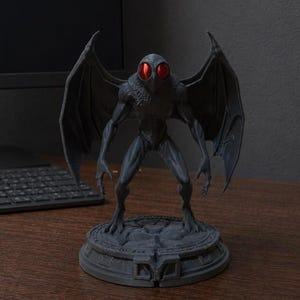 Puede incluir: Una figura de criatura alada gris con grandes ojos rojos brillantes. La figura tiene un pecho texturizado y emplumado, orejas puntiagudas y manos largas con garras. Se apoya sobre una base circular detallada con textura de piedra.