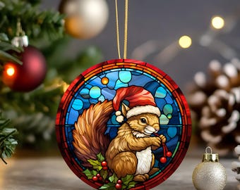 May include: A round Christmas ornament featuring a squirrel wearing a Santa hat, set against a stained-glass style background. The squirrel holds berries, and the ornament has a gold string for hanging. The design incorporates red, brown, and blue colors.