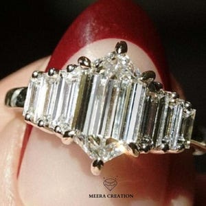 Könnte beinhalten: Ein silberner Ring mit einem Cluster aus klaren, rechteckig geschliffenen Edelsteinen. Der Ring hat einen zentralen Stein im Marquise-Schliff, der von einer Reihe von Baguette-Steinen flankiert wird. Der Ring ist vor einem unscharfen Hintergrund platziert.