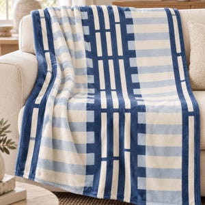 May include: A soft plush throw blanket featuring a geometric pattern of deep navy blue and light blue stripes against a cream background. The design includes vertical bands of solid navy blue with rectangular cutouts and horizontal stripes.