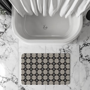 Puede incluir: Una alfombra de baño estampada con un diseño geométrico en tonos grises, negros y beige se coloca frente a una bañera blanca. El diseño de la alfombra presenta formas de diamante con detalles florales. Cortinas de ducha blancas cuelgan sobre la bañera.