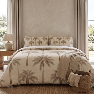 May include: A bedding set featuring a beige duvet cover and two matching pillowcases with a brown palm tree print. A textured beige throw blanket is draped over the foot of the bed, and a woven wicker basket sits on the floor nearby.
