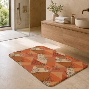 May include: A rectangular bath mat featuring a geometric pattern of triangles in shades of orange, terracotta, and cream. The design is overlaid with a delicate, thin black line drawing of botanical sprigs and leaves across the surface.