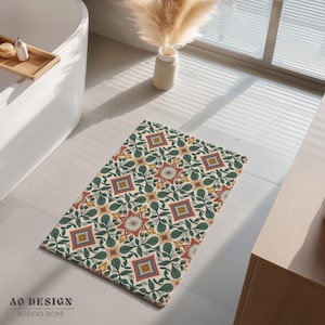 May include: A rectangular bath mat with a cream background and a repeating pattern of green leaves, red and yellow flowers, and square geometric shapes. The mat is placed on a tiled floor near a bathtub. The text "AO DESIGN MODERN HOME" is at the bottom.