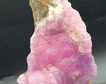 May include: A vibrant pink mineral specimen with a textured, crystalline surface. The stone features a mix of light and deep pink hues, with a section of tan-colored rock at the top. The overall shape is irregular, showcasing natural formations.