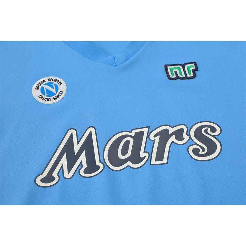 May include: Light blue v-neck jersey with the word "Mars" in large, dark blue letters with a white outline. Features a patch with the letters "nr" and a circular emblem with text "Societa Sportiva Calcio Napoli".