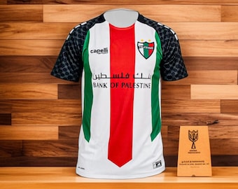 May include: White, red, and green soccer jersey with the text "Bank of Palestine" and the Capelli Sport logo. The jersey has a geometric pattern on the sleeves and a crest with the word "Palestine".