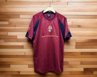 May include: Maroon short-sleeved jersey with navy blue accents. The jersey features a skull graphic and the text "THE FINAL FRONTIER" in gold. The jersey is hanging on a wooden hanger against a wood-paneled wall.