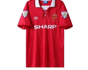 May include: Red soccer jersey with white collar and SHARP logo. Features a lace-up neckline, team crest, and sponsor logos. The jersey has short sleeves and a textured pattern.